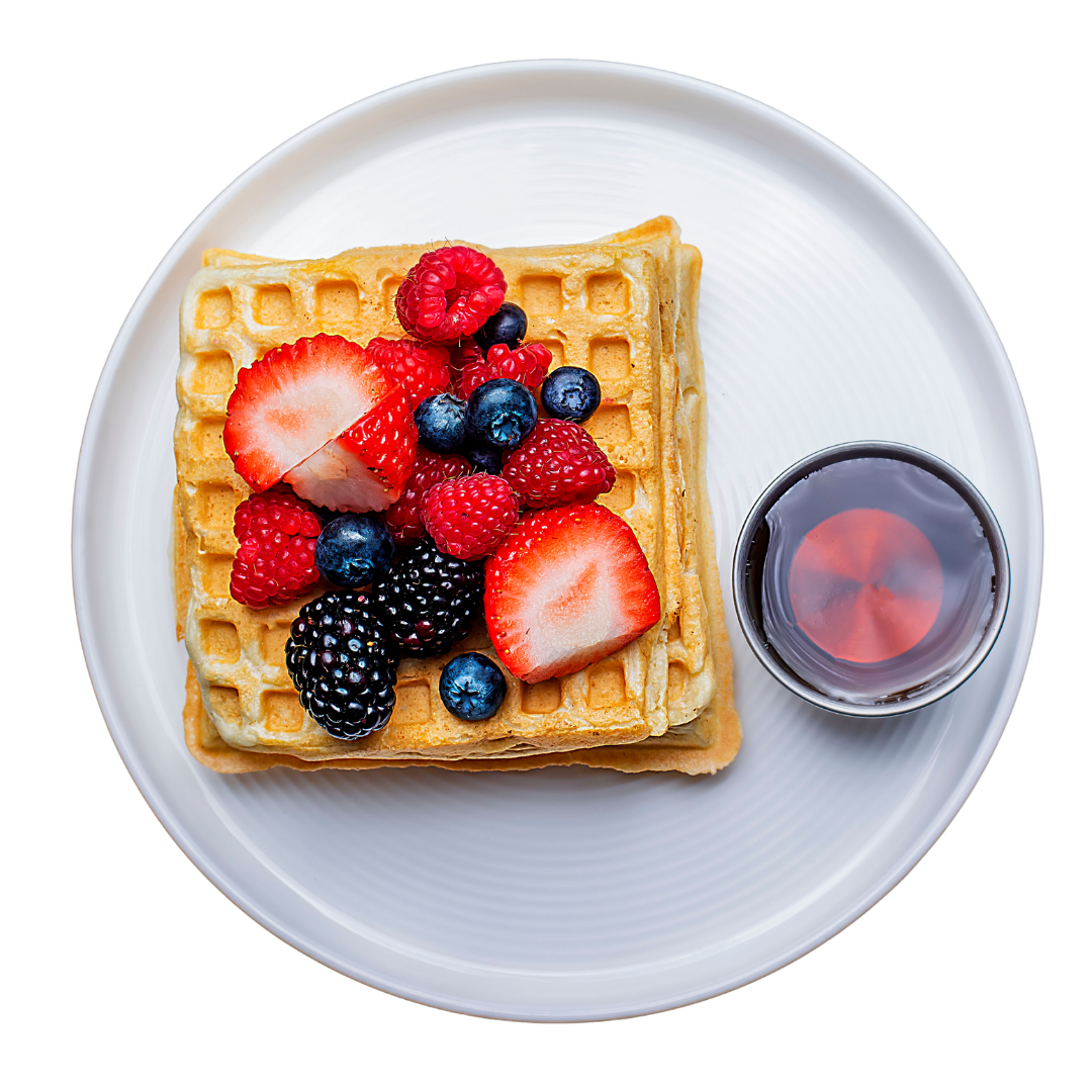 Stack of two golden-brown waffles on a white plate, topped with a variety of fresh berries including strawberries, blueberries, and raspberries, accompanied by a drizzle of maple syrup.